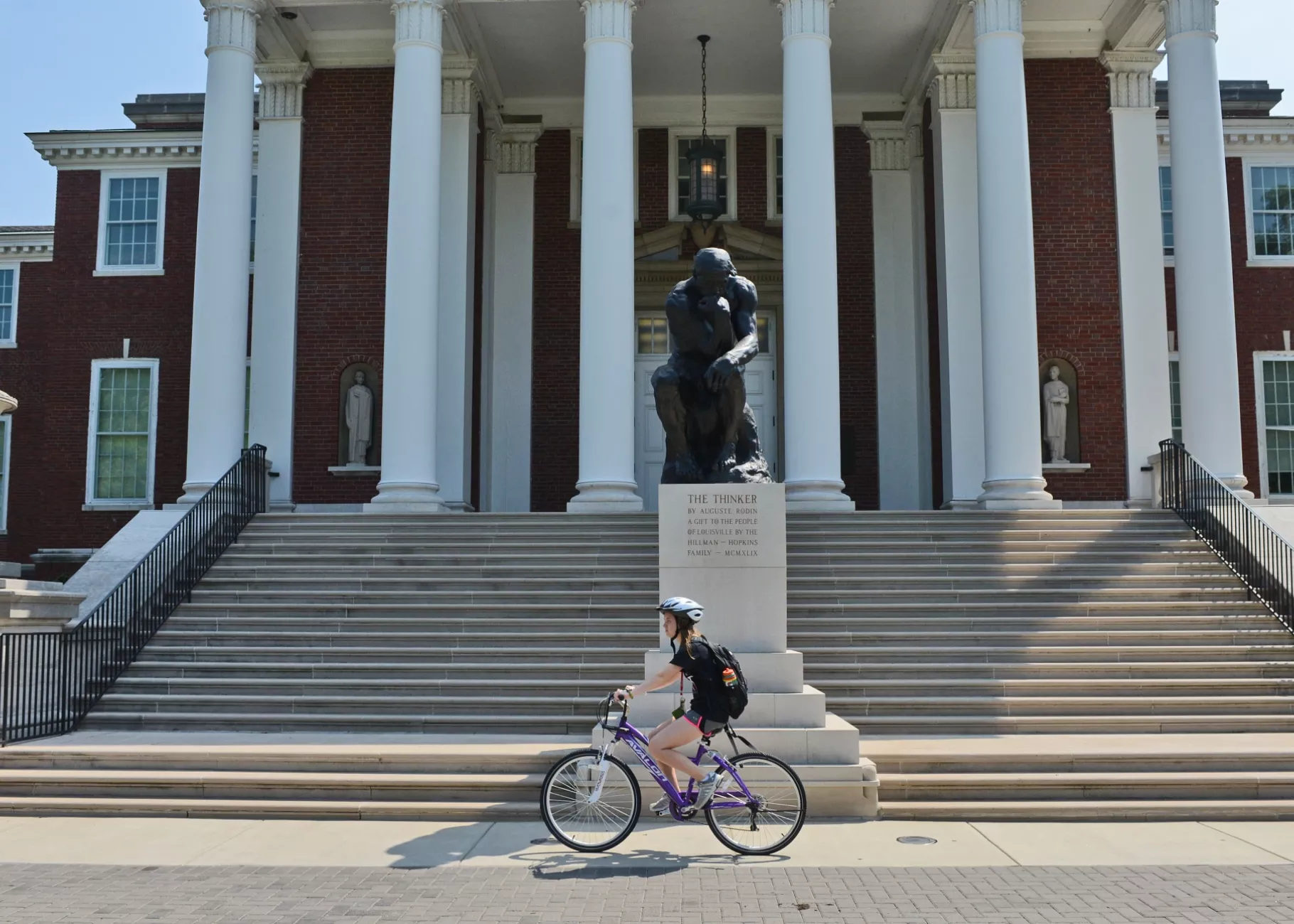 Student biking past the Thinker in front of Grawemeyer Hall