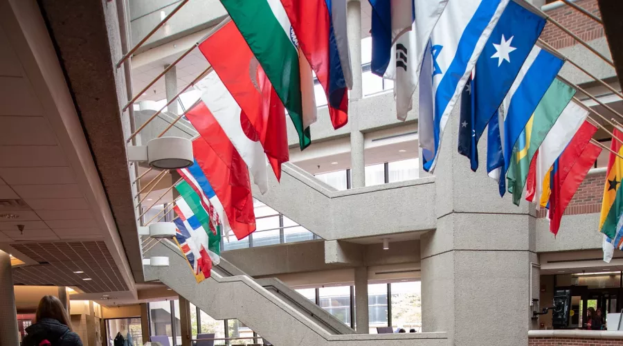 International flags displayed over the common lobby of Frazier Hall with students walking by.