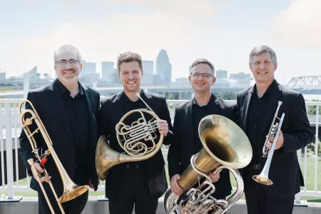 Four members of brass faculty with city backdrop